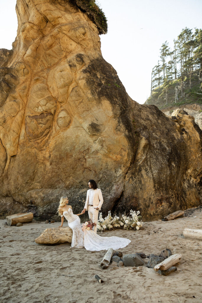 bride sitting on rock and holding hands with groom