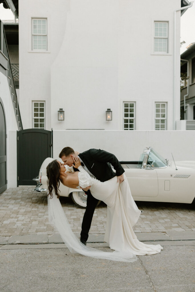 bride and groom dip pose in front of vintage car