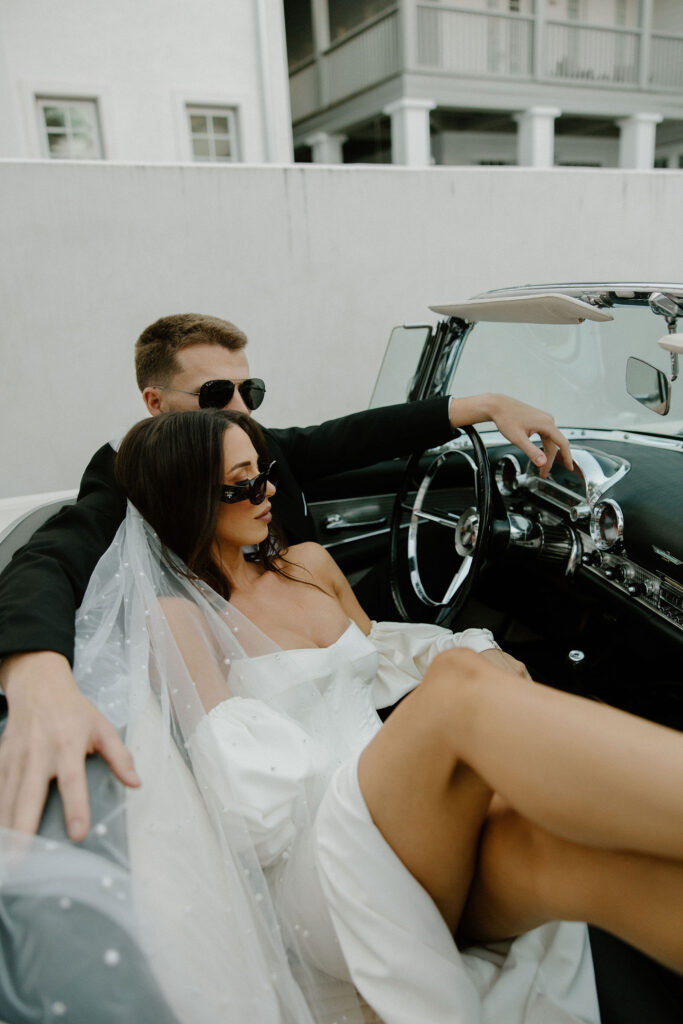 bride and groom posing in vintage car with sunglasses on